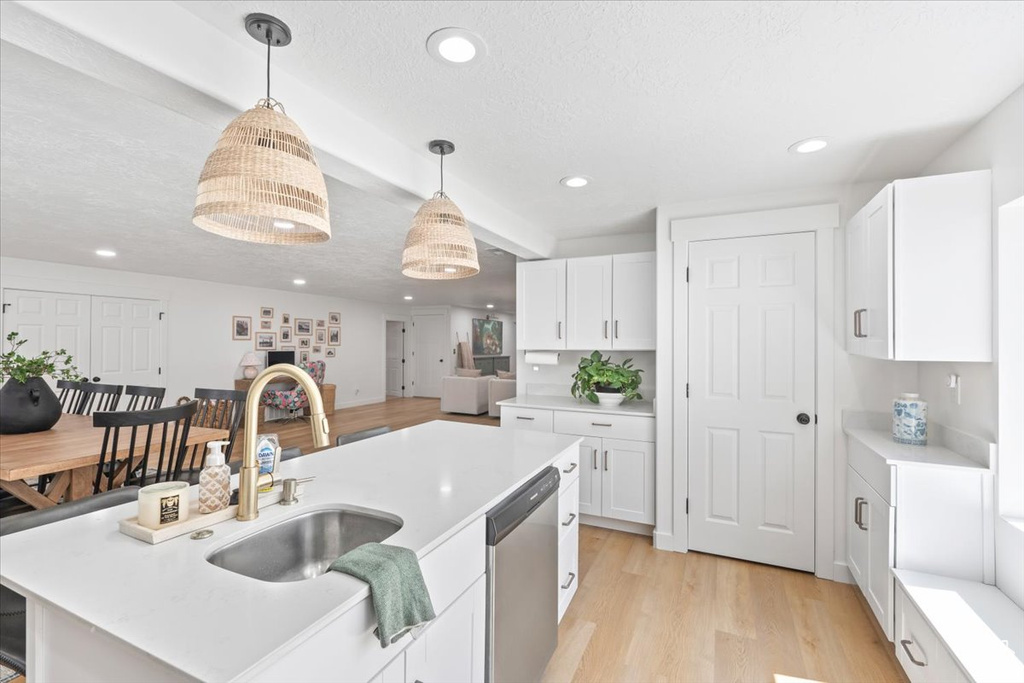 Kitchen with stainless steel dishwasher, white cabinetry, light countertops, decorative light fixtures, and recessed lighting