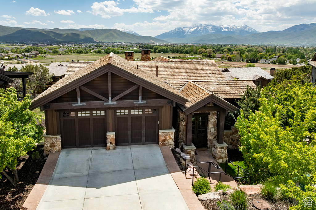 View of front of property with stone siding, a mountain view, driveway, and a garage