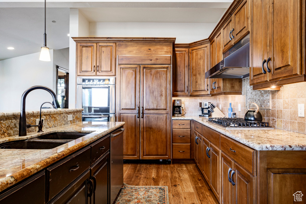 Kitchen featuring under cabinet range hood, stainless steel appliances, dark wood-style floors, light stone counters, and tasteful backsplash