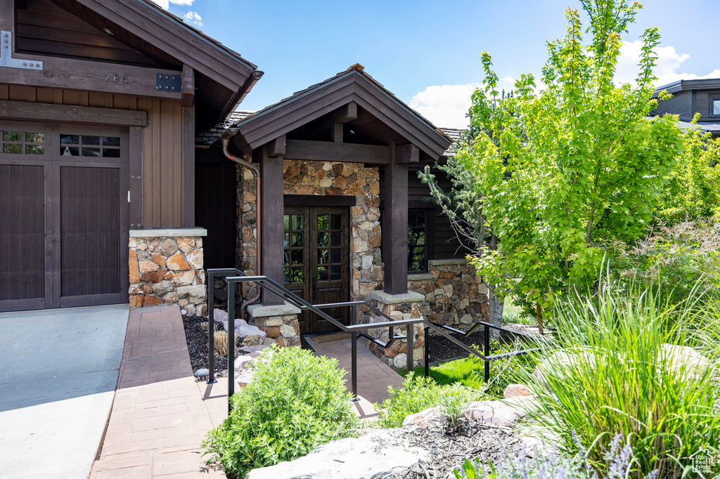 View of exterior entry with french doors, stone siding, a garage, concrete driveway, and board and batten siding