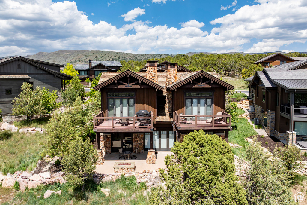 Rear view of property with stone siding, french doors, a patio, a chimney, and a deck with mountain view