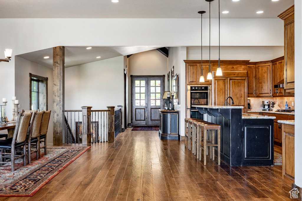 Kitchen featuring brown cabinets, stainless steel appliances, dark wood-style floors, a breakfast bar, and recessed lighting