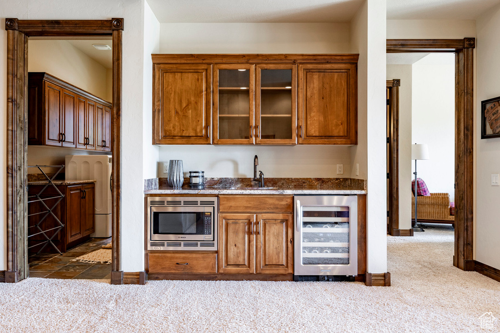 Indoor wet bar featuring wine cooler, stainless steel microwave, and dark colored carpet