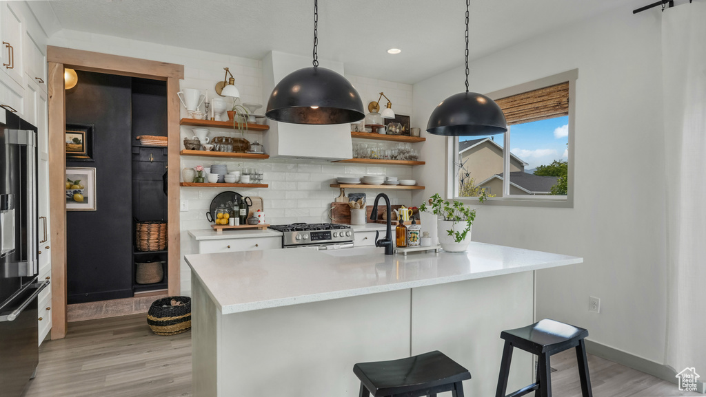 Kitchen with stainless steel gas range oven, backsplash, light wood-style flooring, open shelves, and recessed lighting