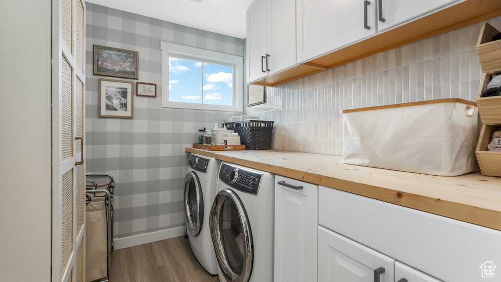 Laundry room with cabinet space, independent washer and dryer, wood finished floors, and wallpapered walls