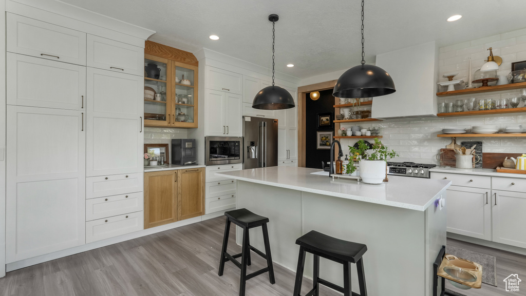 Kitchen with open shelves, appliances with stainless steel finishes, light countertops, decorative backsplash, and a breakfast bar area