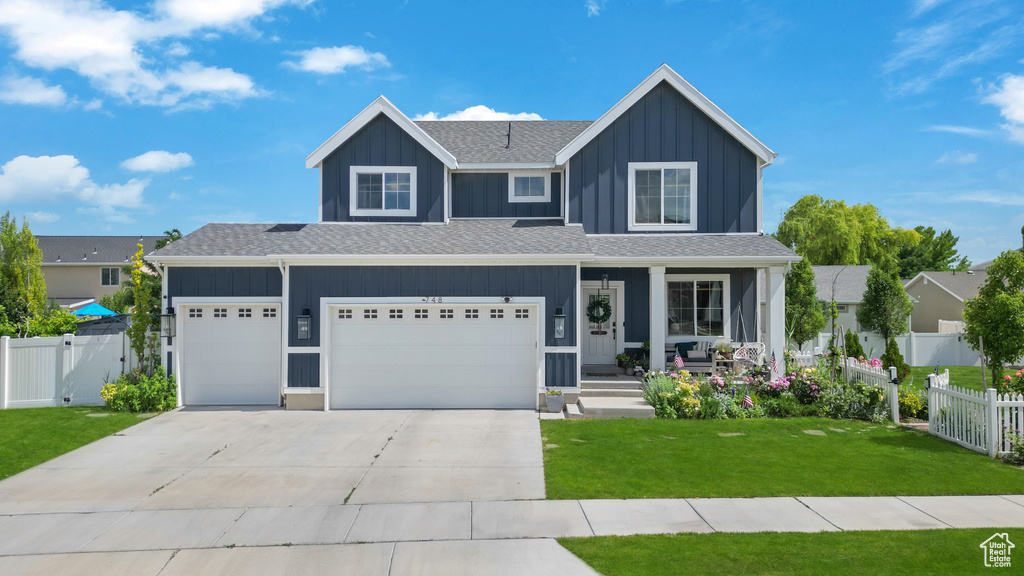 View of front facade with covered porch, board and batten siding, concrete driveway, a garage, and roof with shingles