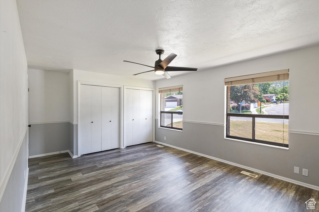 Unfurnished bedroom featuring multiple closets, dark wood finished floors, baseboards, a textured ceiling, and a ceiling fan