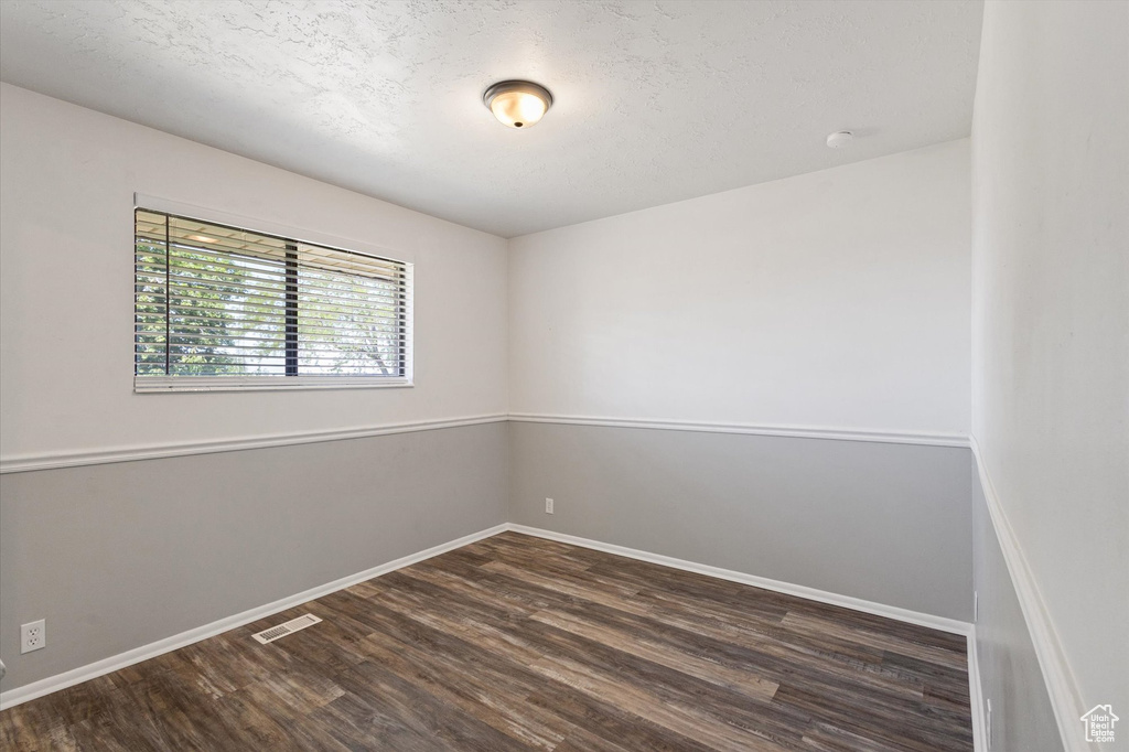Spare room featuring dark wood-style floors, baseboards, and a textured ceiling