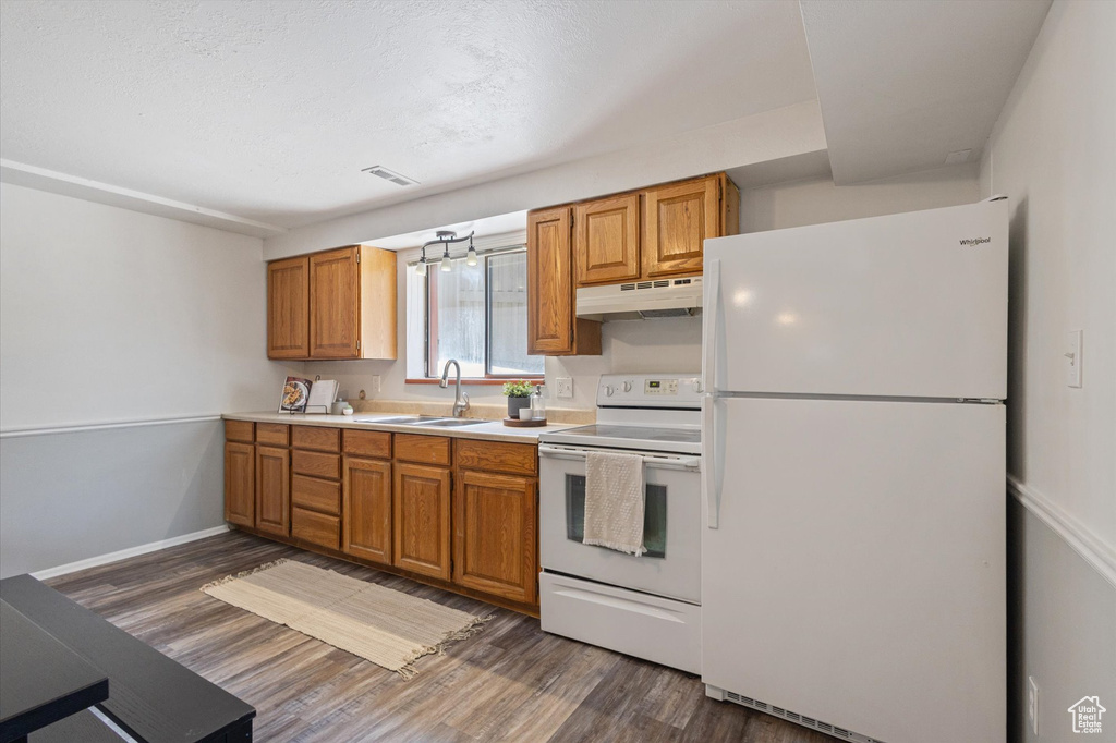 Kitchen featuring white appliances, under cabinet range hood, a sink, dark wood-style flooring, and light countertops
