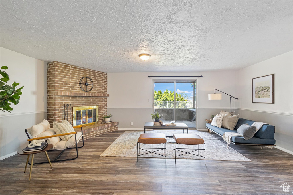 Living room with a textured ceiling, wood finished floors, a brick fireplace, and baseboards