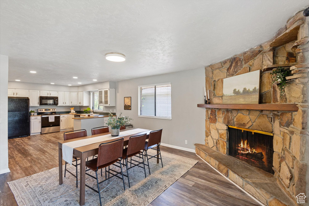 Dining area featuring baseboards, wood finished floors, a stone fireplace, and recessed lighting