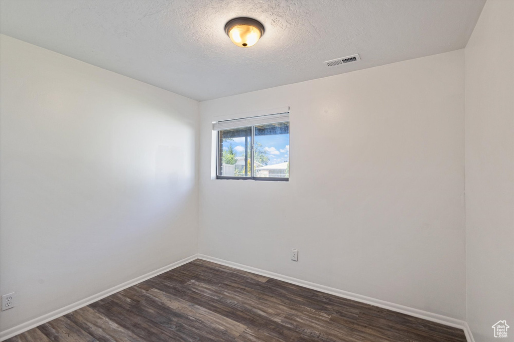 Empty room featuring dark wood-type flooring, baseboards, and a textured ceiling