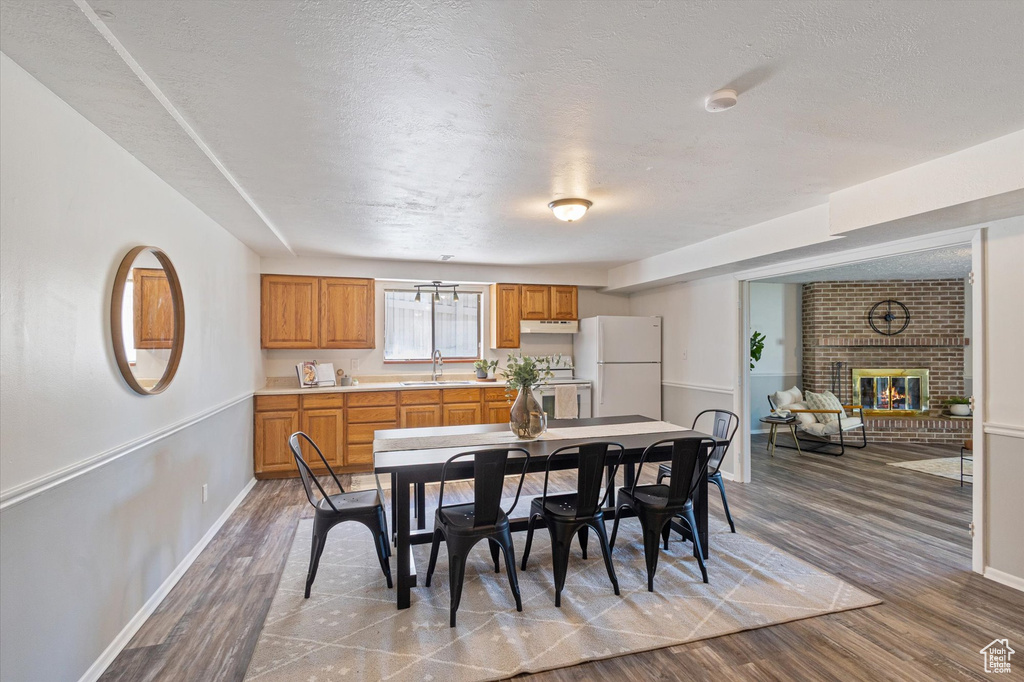 Dining space featuring a brick fireplace, wood finished floors, baseboards, and a textured ceiling