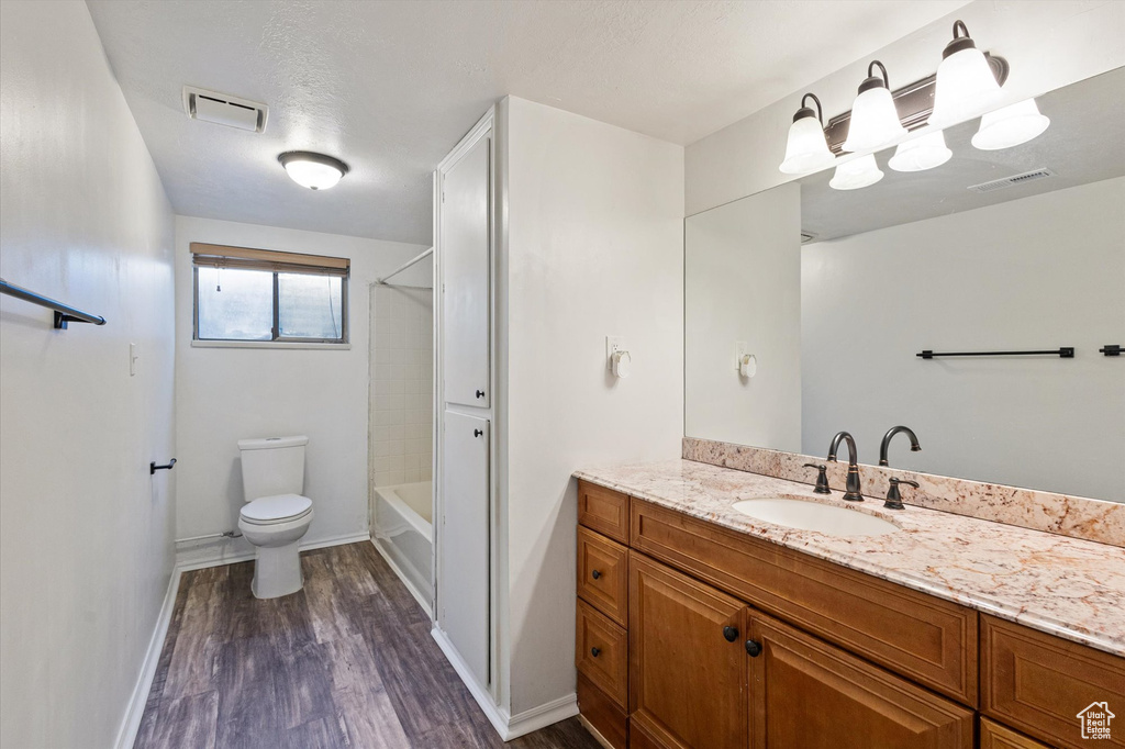 Bathroom featuring vanity, wood finished floors, toilet, baseboards, and shower / tub combination