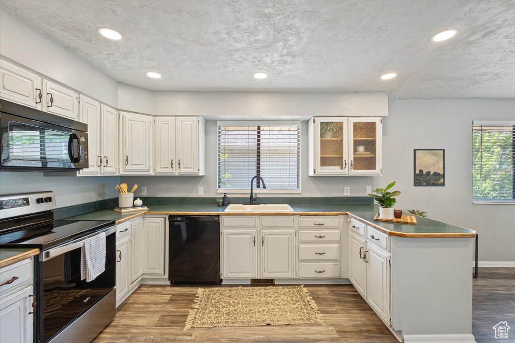 Kitchen with black appliances, a sink, a peninsula, dark countertops, and wood finished floors