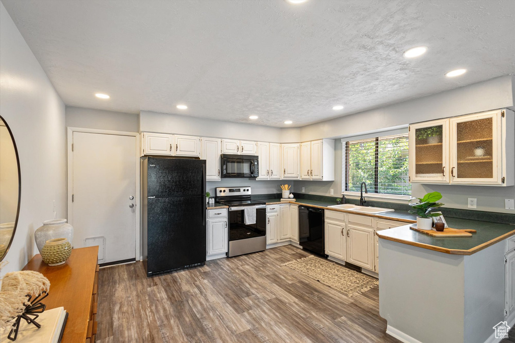 Kitchen with black appliances, a sink, dark wood-style flooring, dark countertops, and recessed lighting