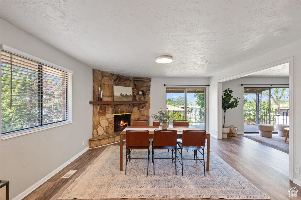 Dining room featuring a textured ceiling, wood finished floors, a stone fireplace, and baseboards