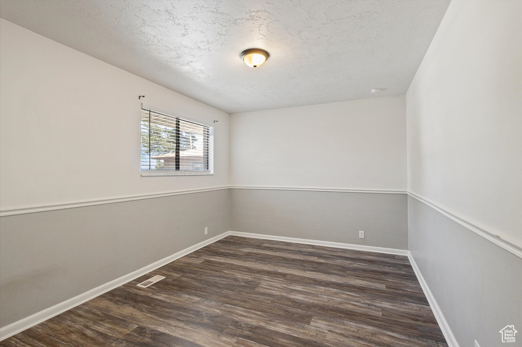 Empty room with a textured ceiling, wood finished floors, and baseboards