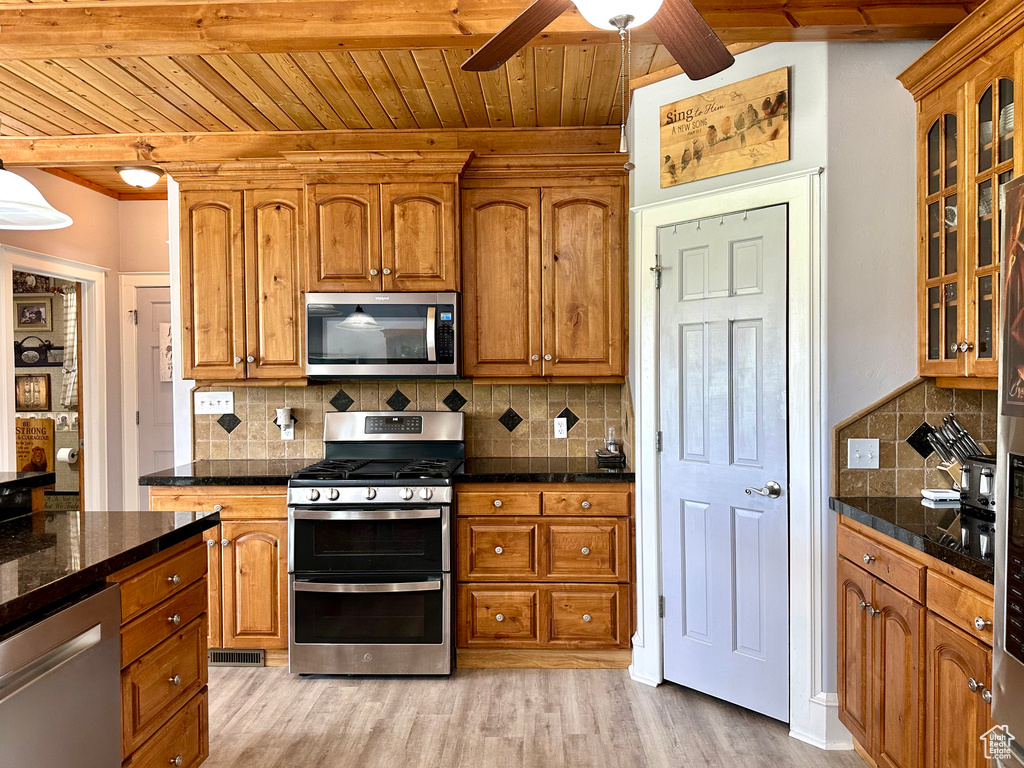Kitchen with appliances with stainless steel finishes, wooden ceiling, ceiling fan, glass insert cabinets, and tasteful backsplash