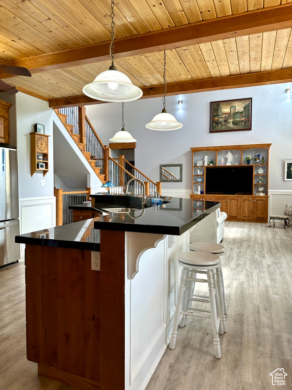 Kitchen featuring freestanding refrigerator, wood ceiling with exposed beams, dark countertops, light wood finished floors, and a sink