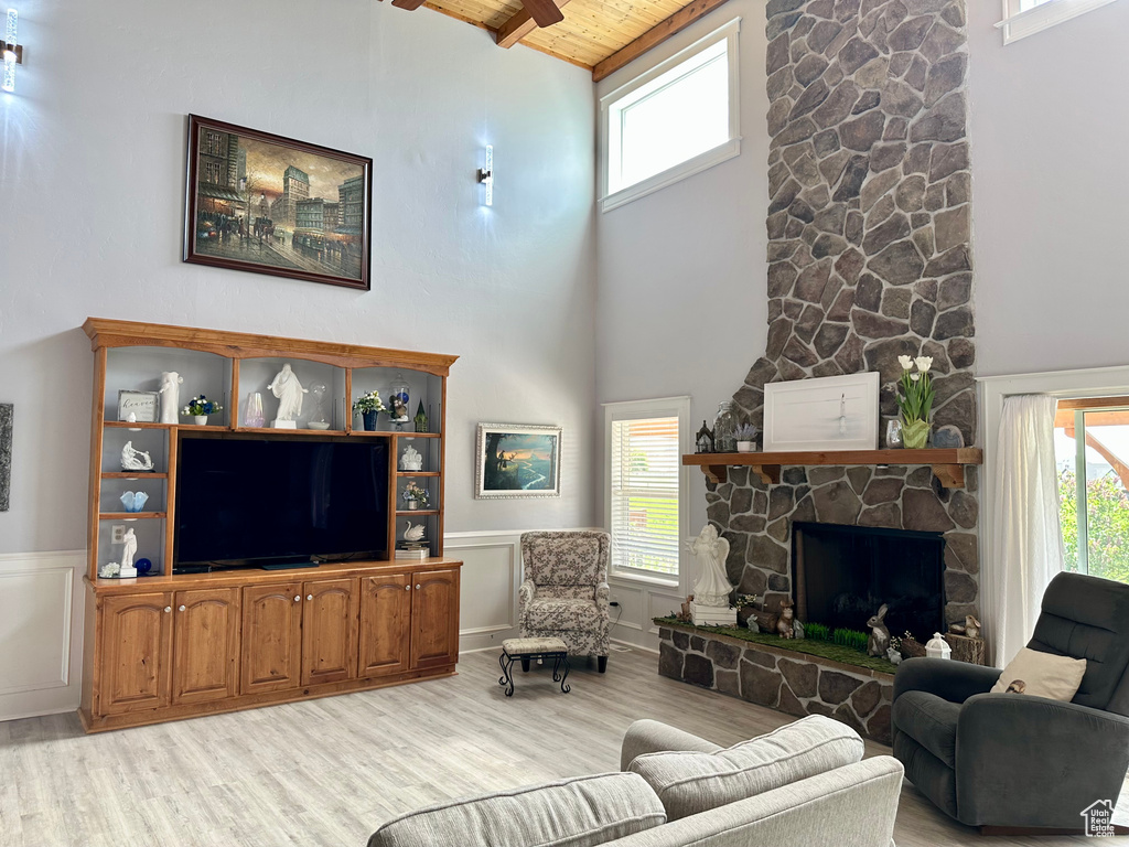 Living room featuring light wood-style flooring, wooden ceiling with exposed beams, high vaulted ceiling, wainscoting, and a fireplace