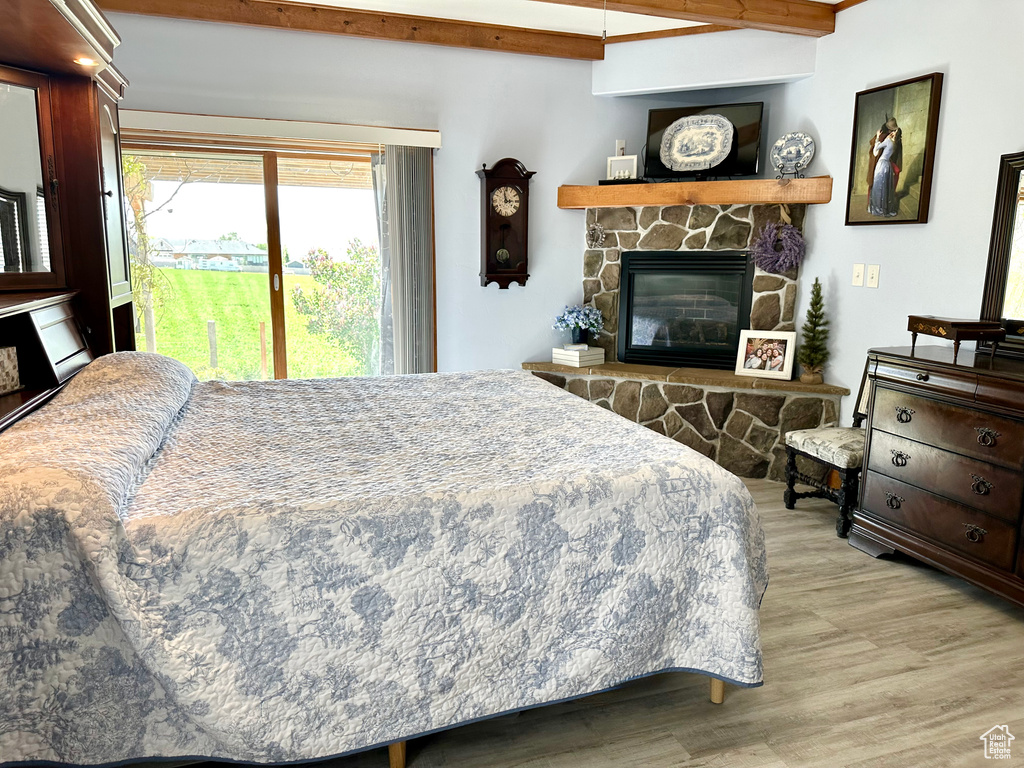 Bedroom with wood finished floors, access to outside, a stone fireplace, and beamed ceiling