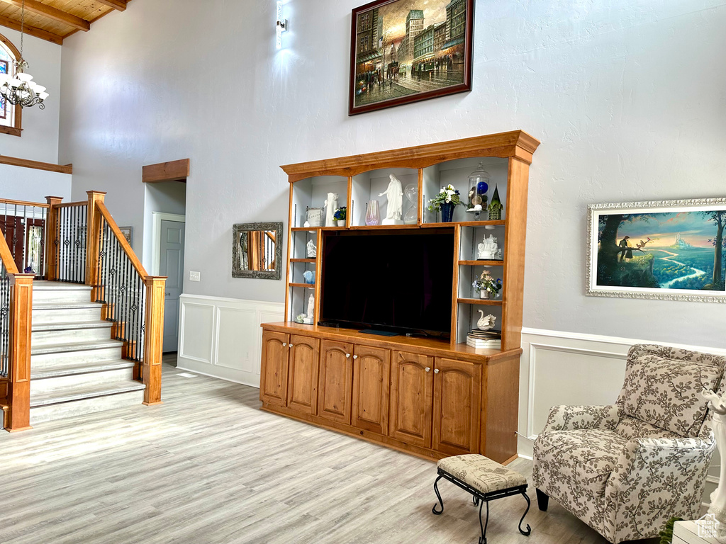 Living area featuring light wood-style flooring, wood ceiling with exposed beams, stairway, a wainscoted wall, and a chandelier