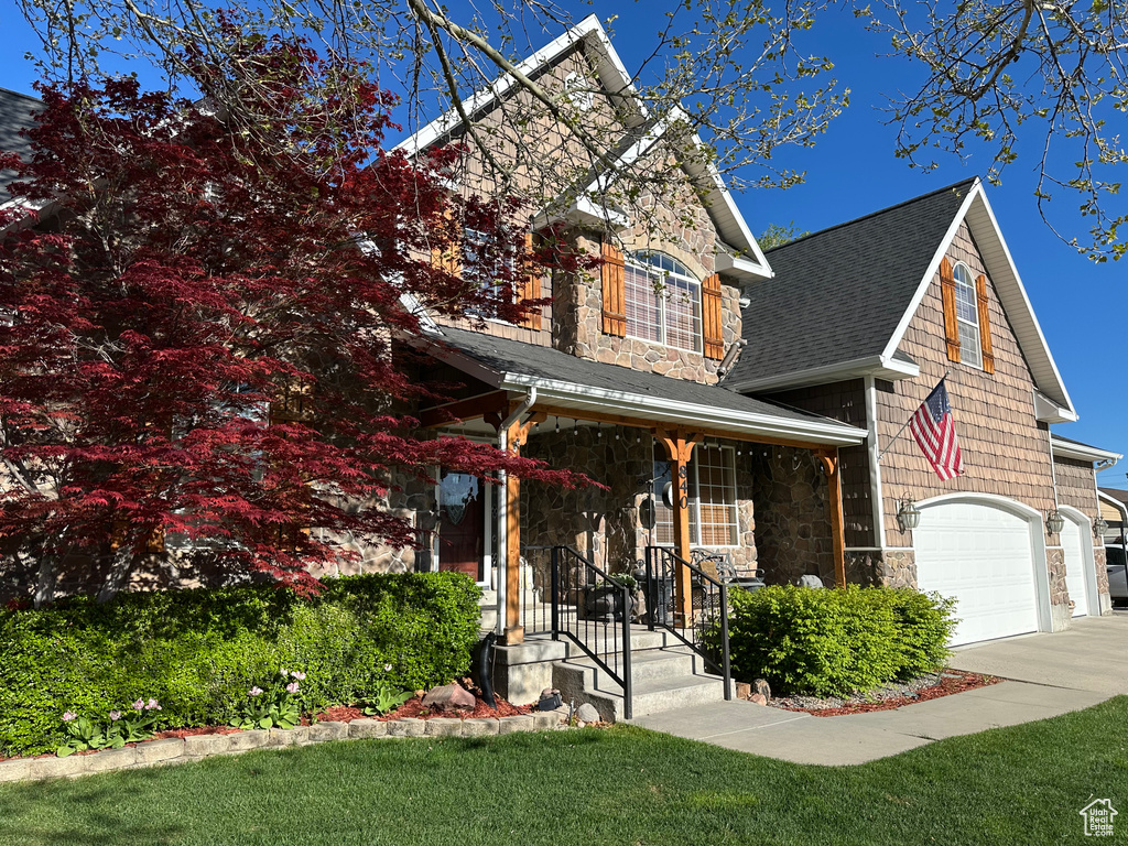View of front of house with stone siding, a garage, roof with shingles, and driveway