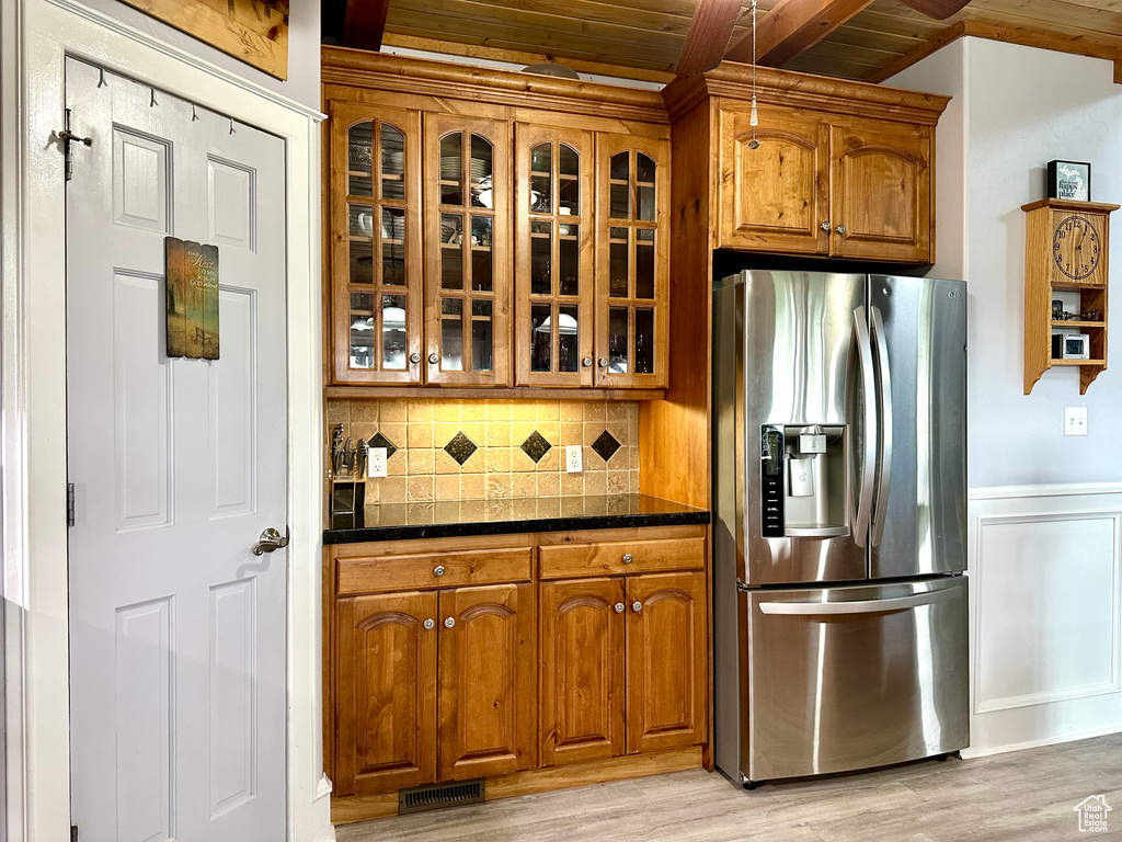 Kitchen with stainless steel refrigerator with ice dispenser, wood ceiling, glass insert cabinets, brown cabinets, and decorative backsplash