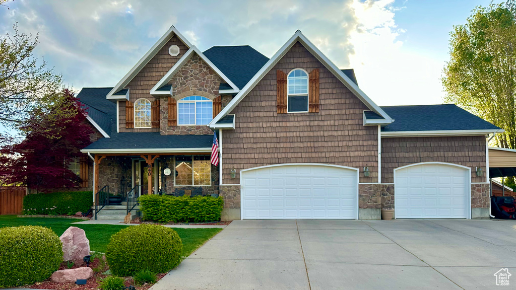 Craftsman-style house with stone siding, concrete driveway, an attached garage, covered porch, and roof with shingles