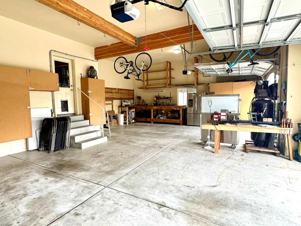 Garage featuring a workshop area, a garage door opener, and stainless steel fridge with ice dispenser