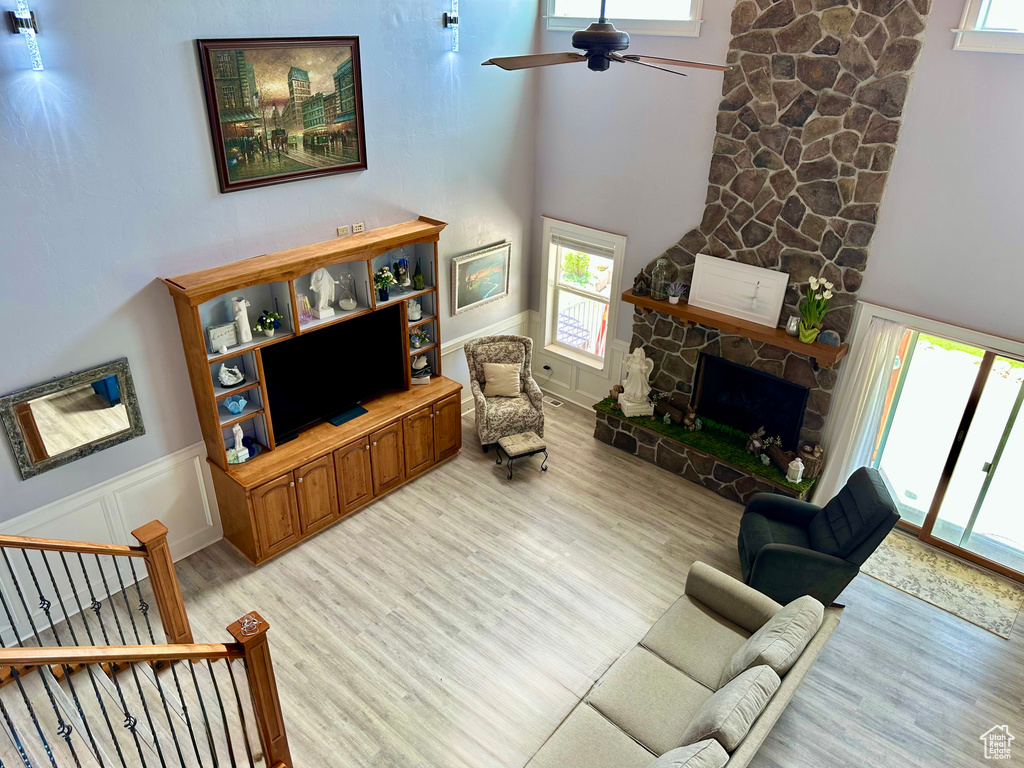 Living area featuring light wood-style flooring, ceiling fan, a towering ceiling, a fireplace, and wainscoting