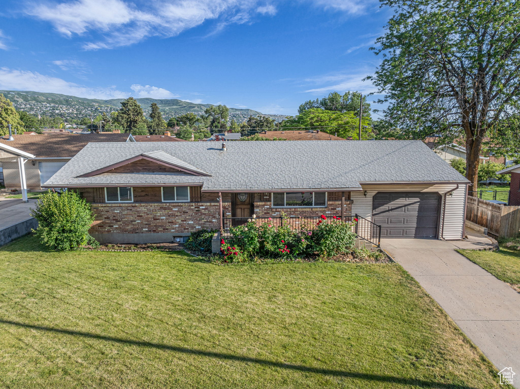 Single story home featuring an attached garage, concrete driveway, a shingled roof, brick siding, and a mountain view