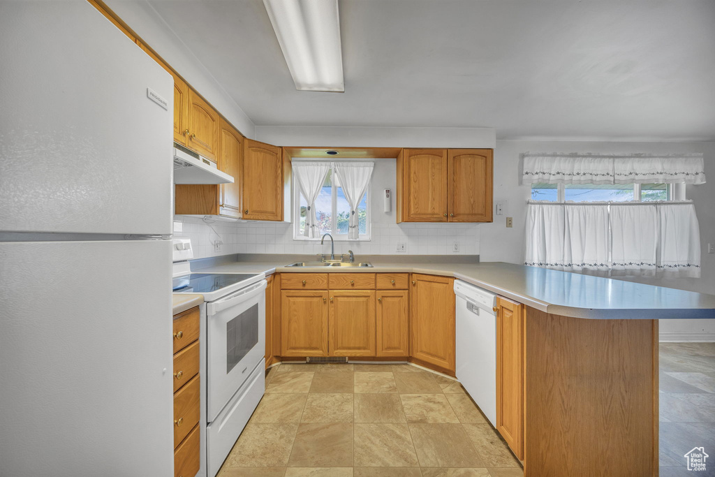 Kitchen with white appliances, a peninsula, under cabinet range hood, and tasteful backsplash