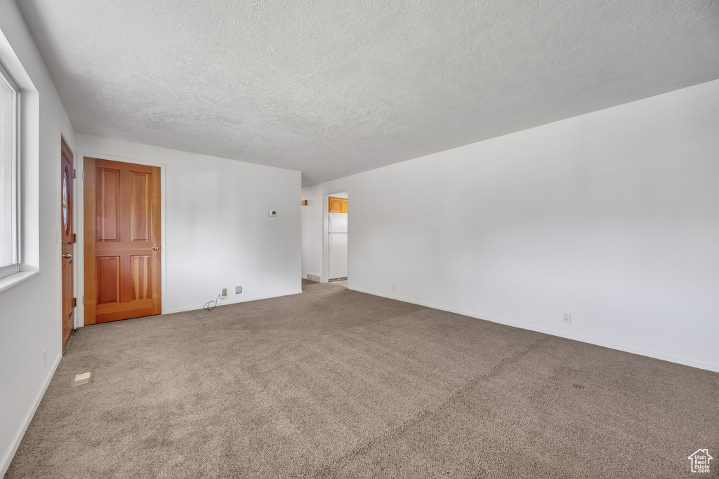 Carpeted spare room featuring a textured ceiling and baseboards