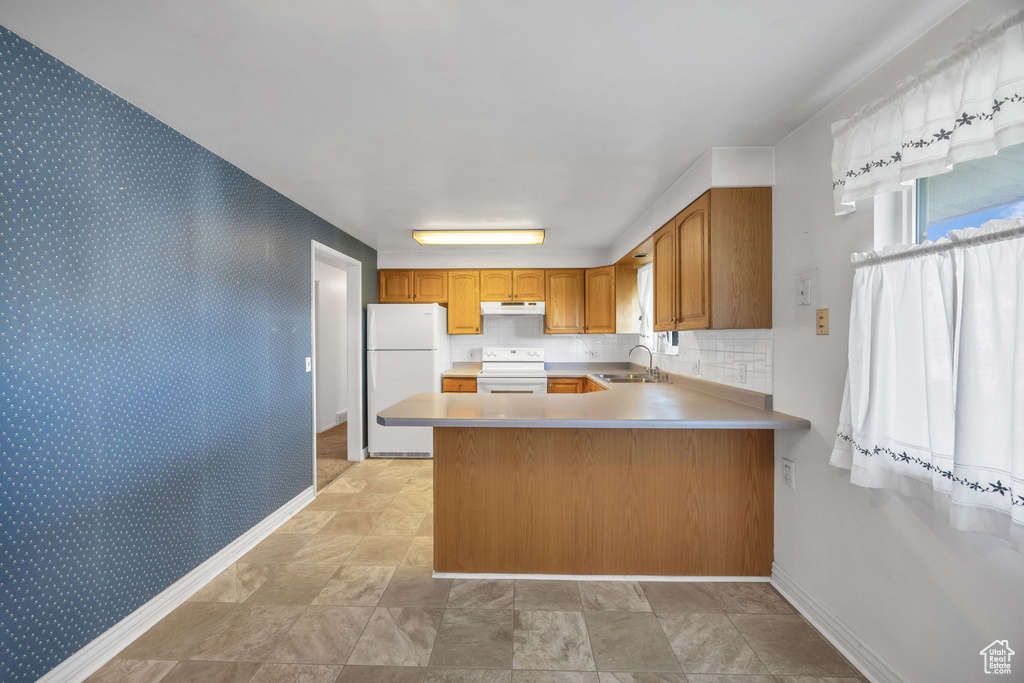 Kitchen with white appliances, a peninsula, under cabinet range hood, light countertops, and brown cabinets