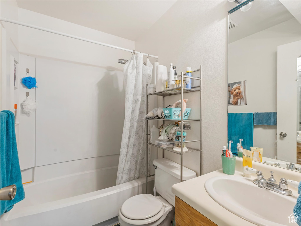 Bathroom featuring vanity, shower / bathtub combination with curtain, and toilet