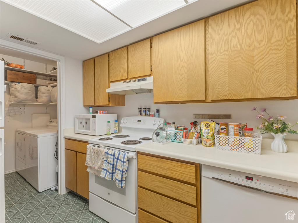 Kitchen with under cabinet range hood, white appliances, washing machine and clothes dryer, light countertops, and light flooring