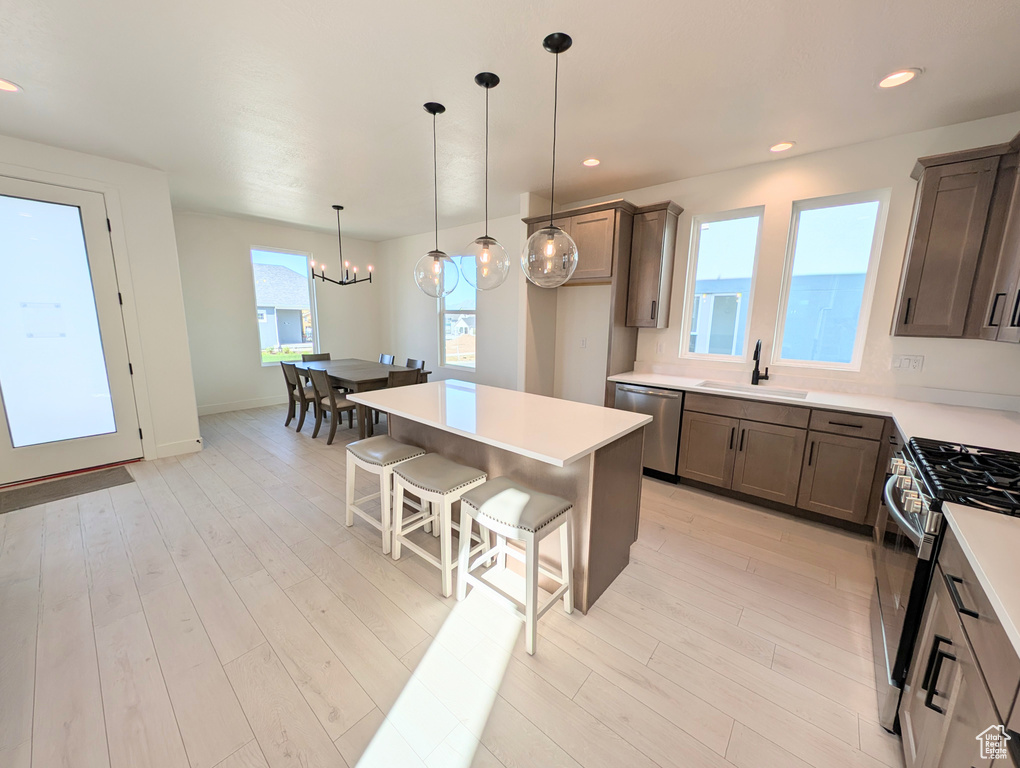 Kitchen featuring stainless steel appliances, a kitchen bar, a chandelier, hanging light fixtures, and light wood-type flooring