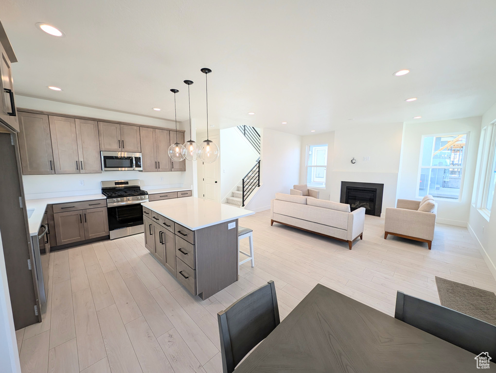 Kitchen featuring stainless steel appliances, light wood finished floors, open floor plan, a kitchen breakfast bar, and light countertops
