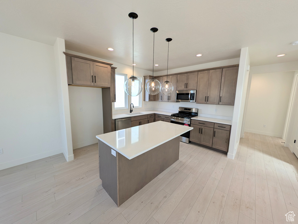 Kitchen with appliances with stainless steel finishes, light countertops, light wood-style flooring, decorative light fixtures, and a center island