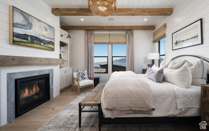 Bedroom with light wood-style floors, beamed ceiling, a glass covered fireplace, and recessed lighting
