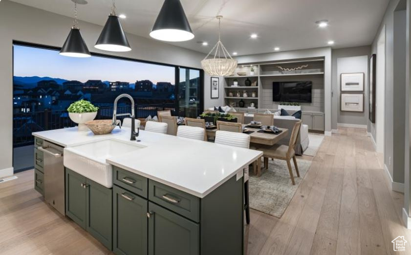 Kitchen with stainless steel dishwasher, open floor plan, light wood-style flooring, light countertops, and an island with sink