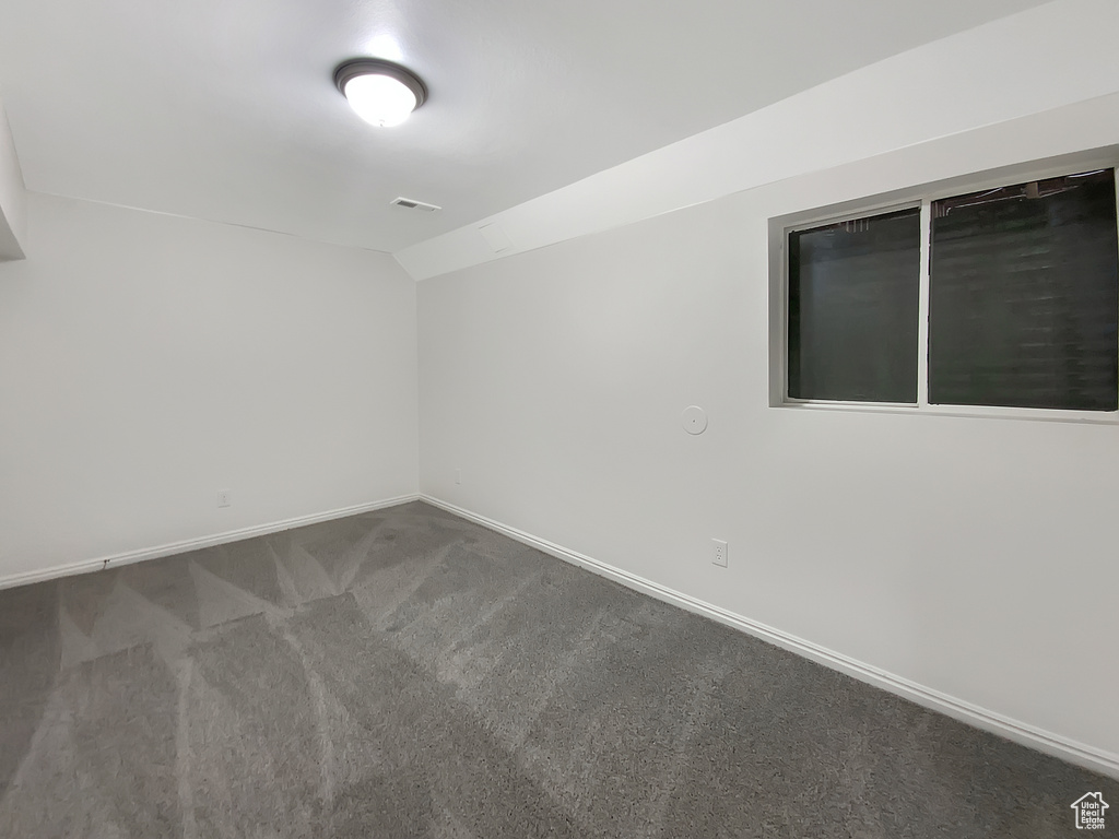 Spare room featuring carpet and vaulted ceiling