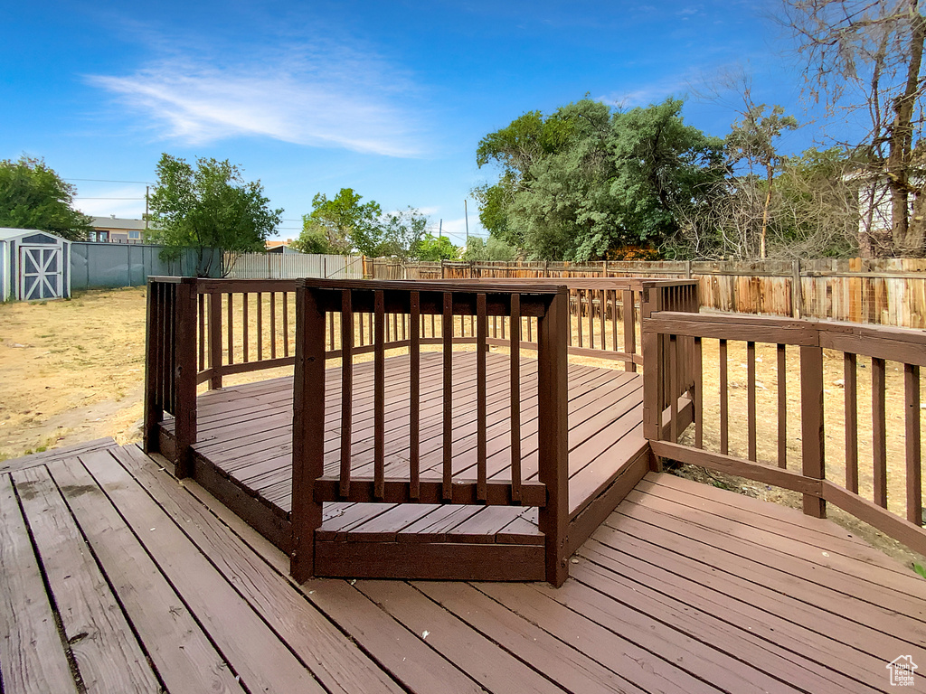 Wooden deck featuring a fenced backyard and a storage unit