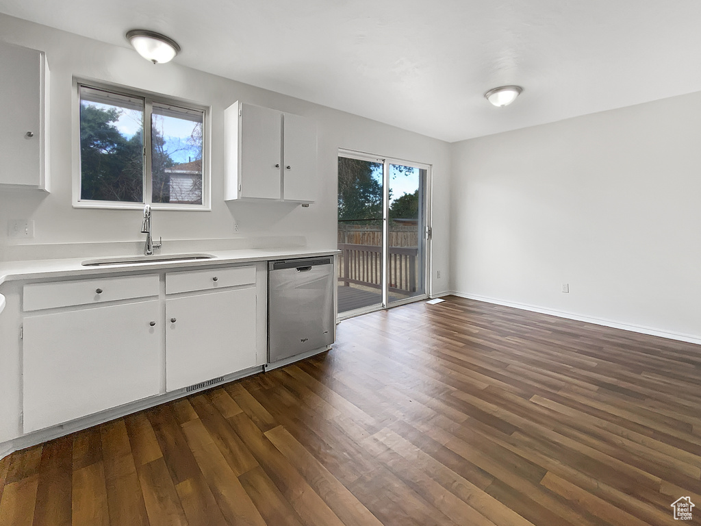 Kitchen with stainless steel dishwasher, dark wood-style flooring, white cabinetry, and light countertops