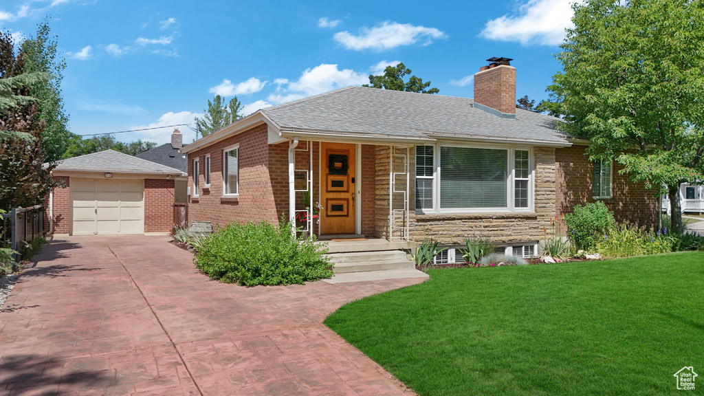 View of front of property with a chimney, a front yard, driveway, brick siding, and an outbuilding