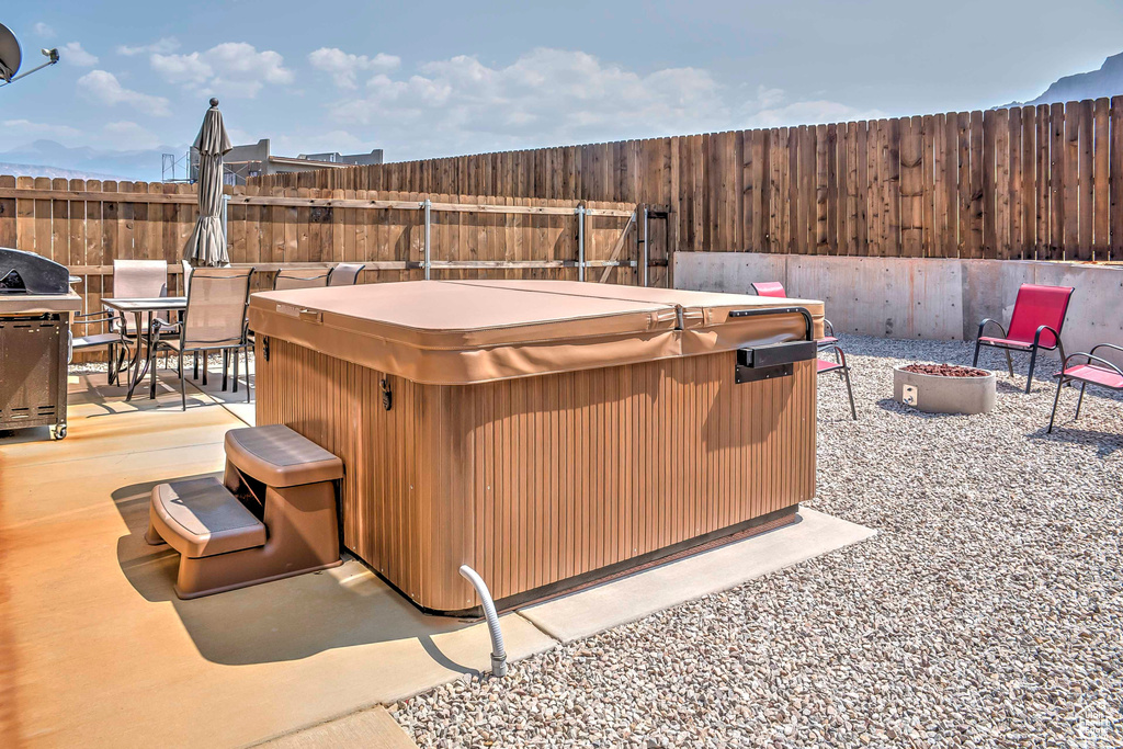 Fenced backyard with a hot tub, an outdoor fire pit, a patio, outdoor dining space, and grilling area