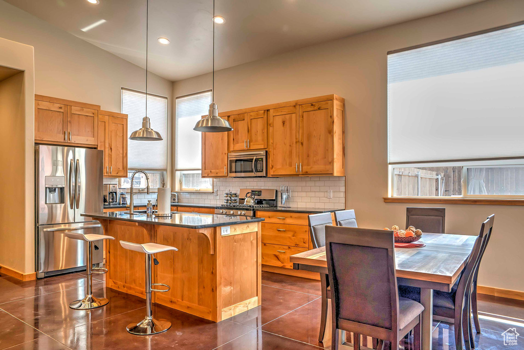 Kitchen featuring stainless steel appliances, dark countertops, a sink, tasteful backsplash, and an island with sink